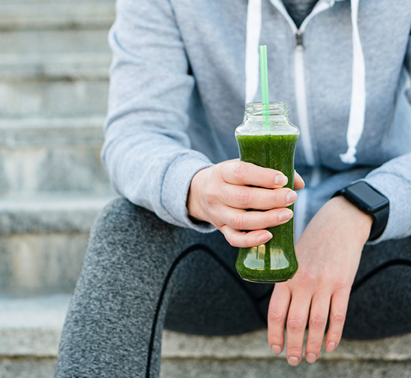 woman in workout attire holding healthy green drink